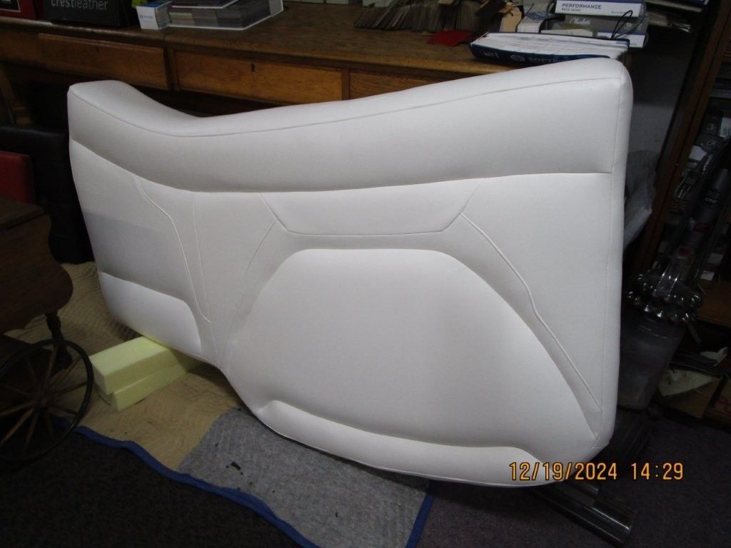 White, contoured motorcycle seat against a cluttered workshop background.