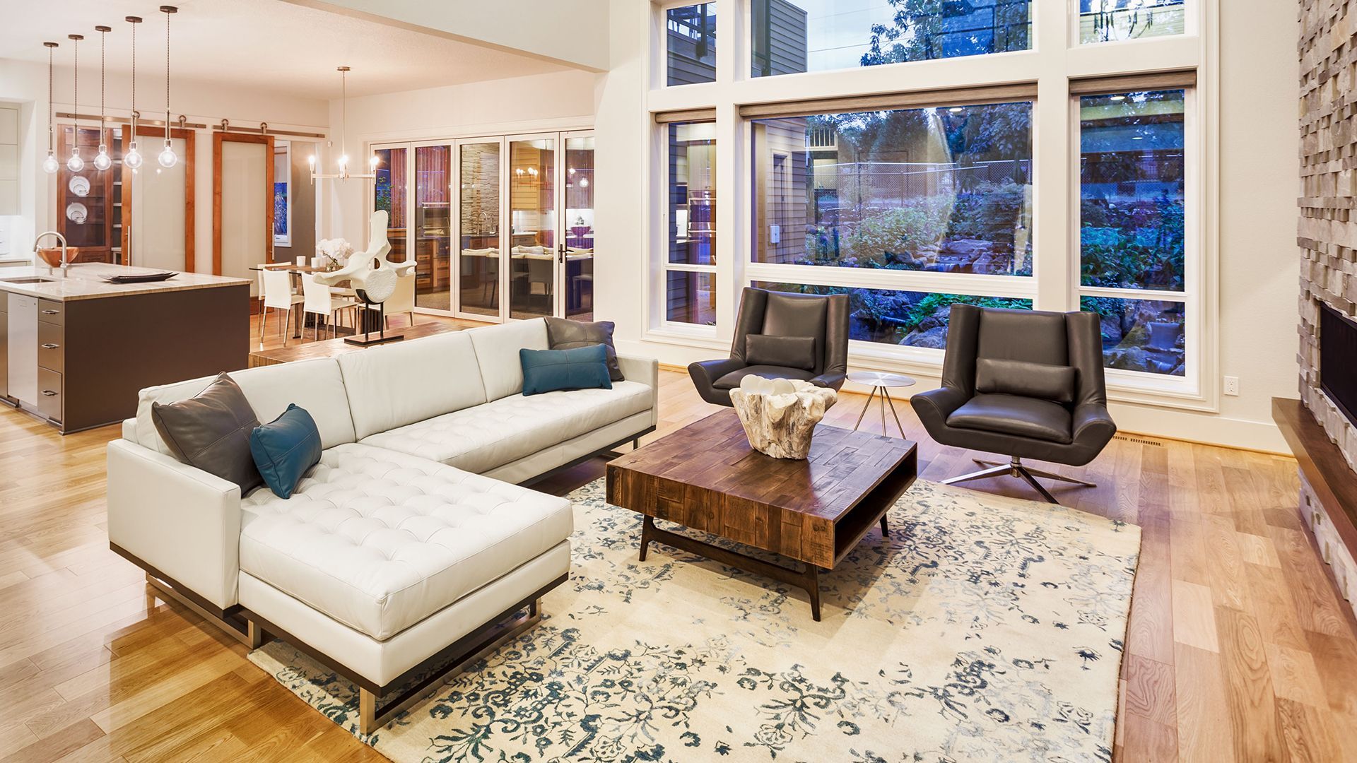 A living room with a couch, chairs, coffee table and large windows.