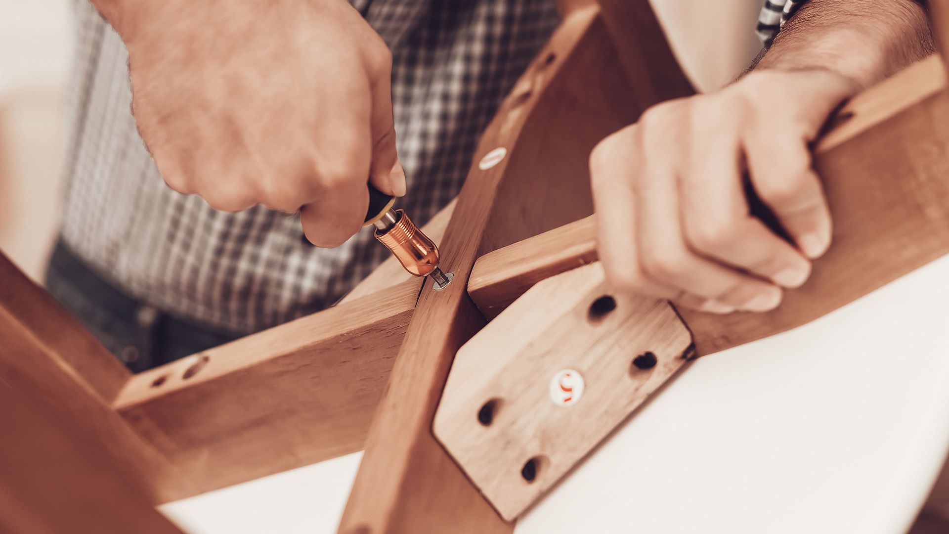 A man is using a screwdriver to assemble a wooden table.