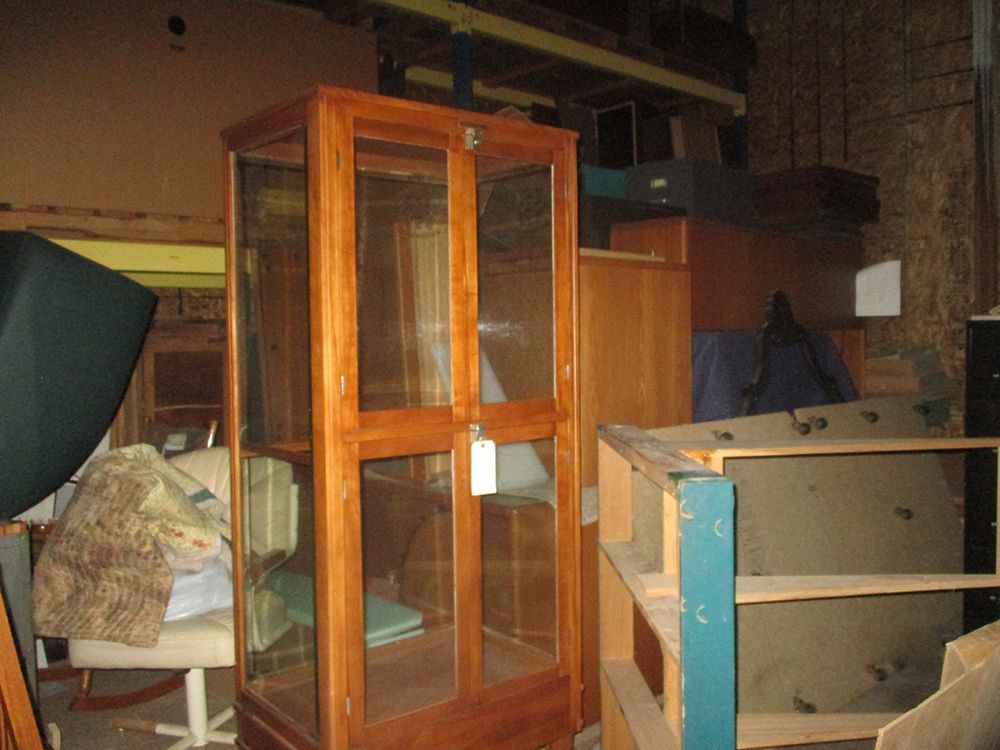 A wooden cabinet with glass doors is sitting in a room filled with lots of furniture.