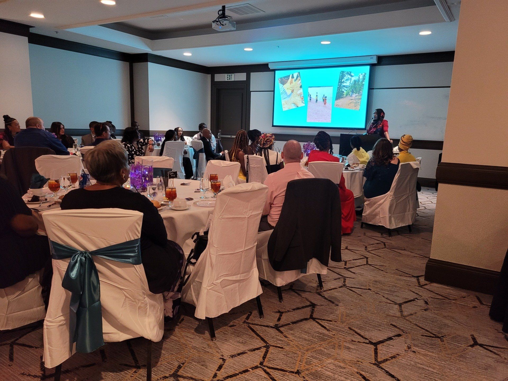 A group of people are sitting at tables in a room watching a presentation.