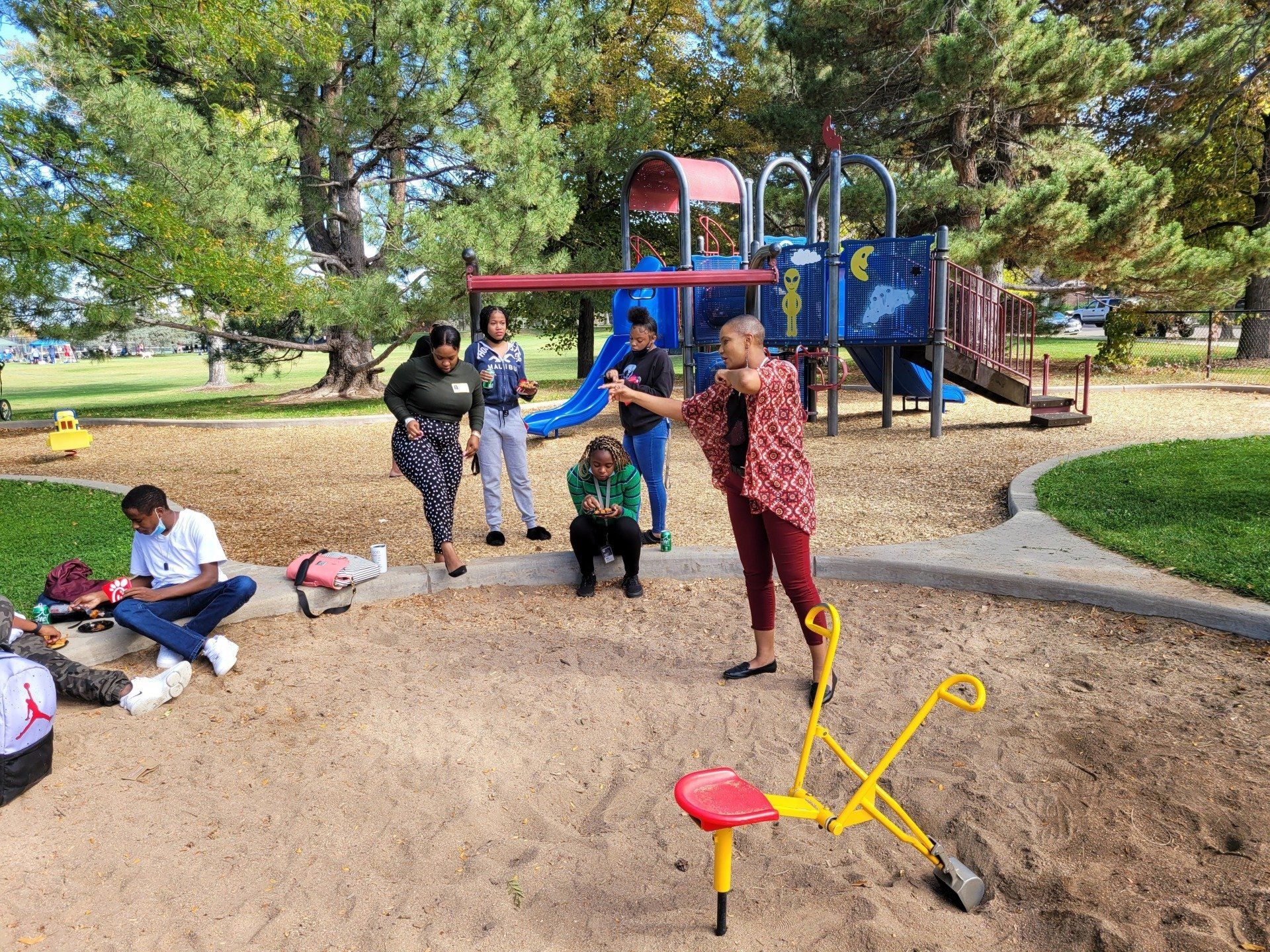 A group of people are standing around a playground in a park.