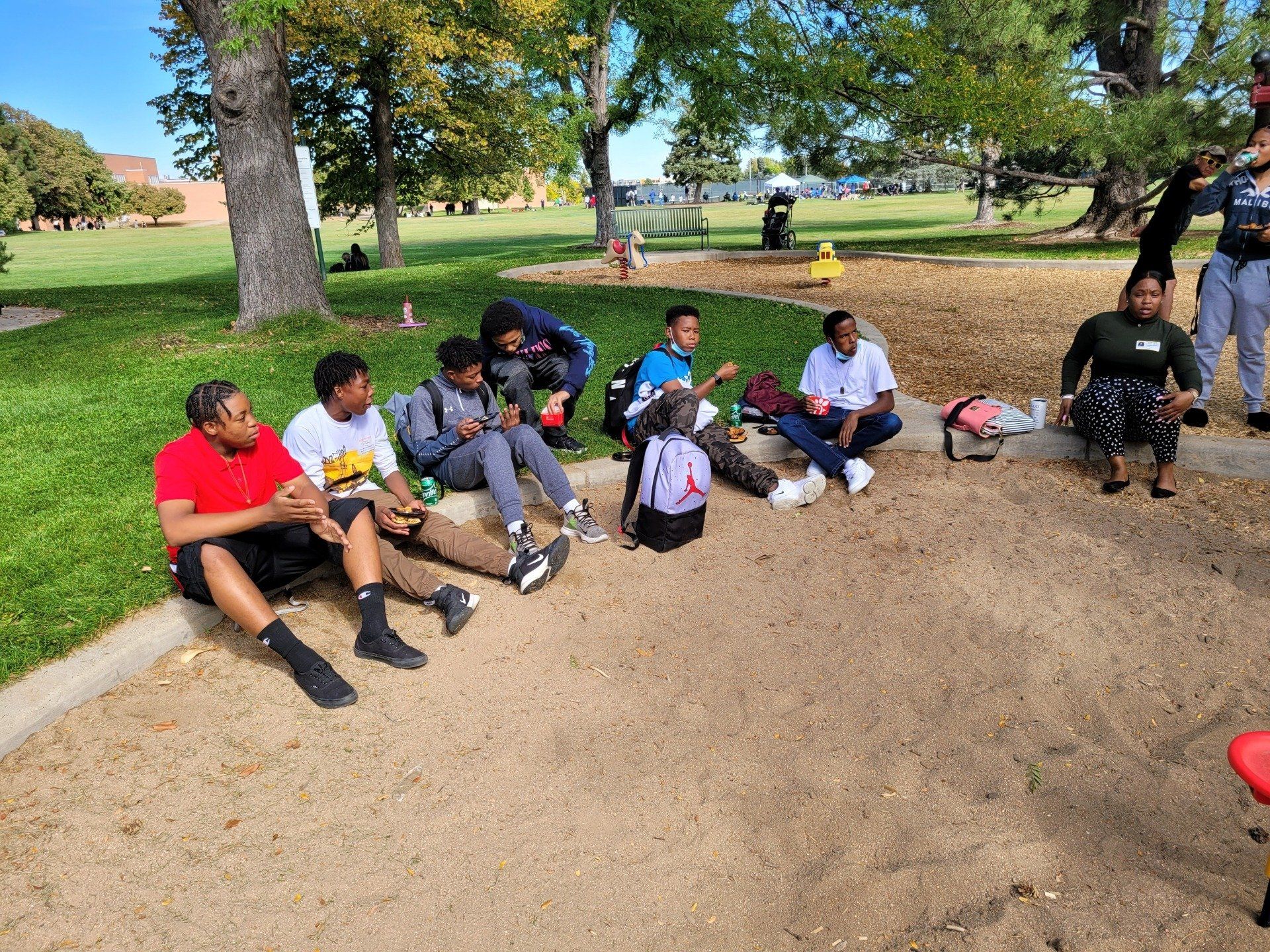 A group of people are sitting on the ground in a park eating food.