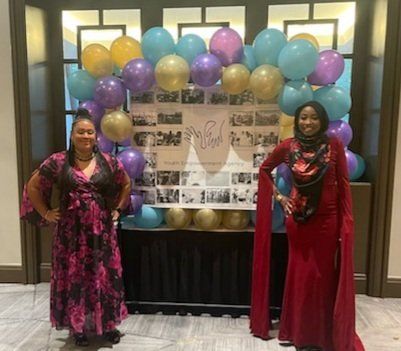 Two women are standing in front of a wall of balloons.