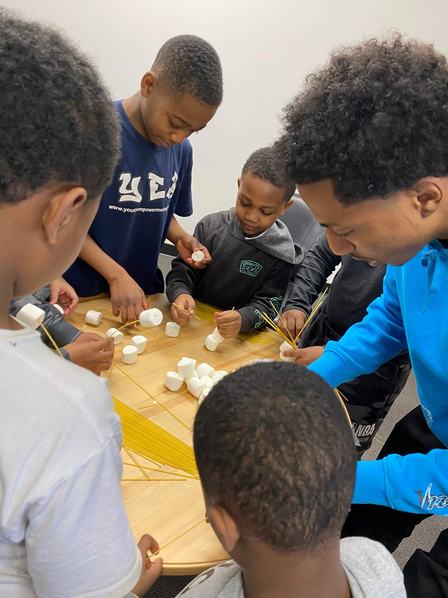 A group of young boys are sitting around a table making marshmallows.