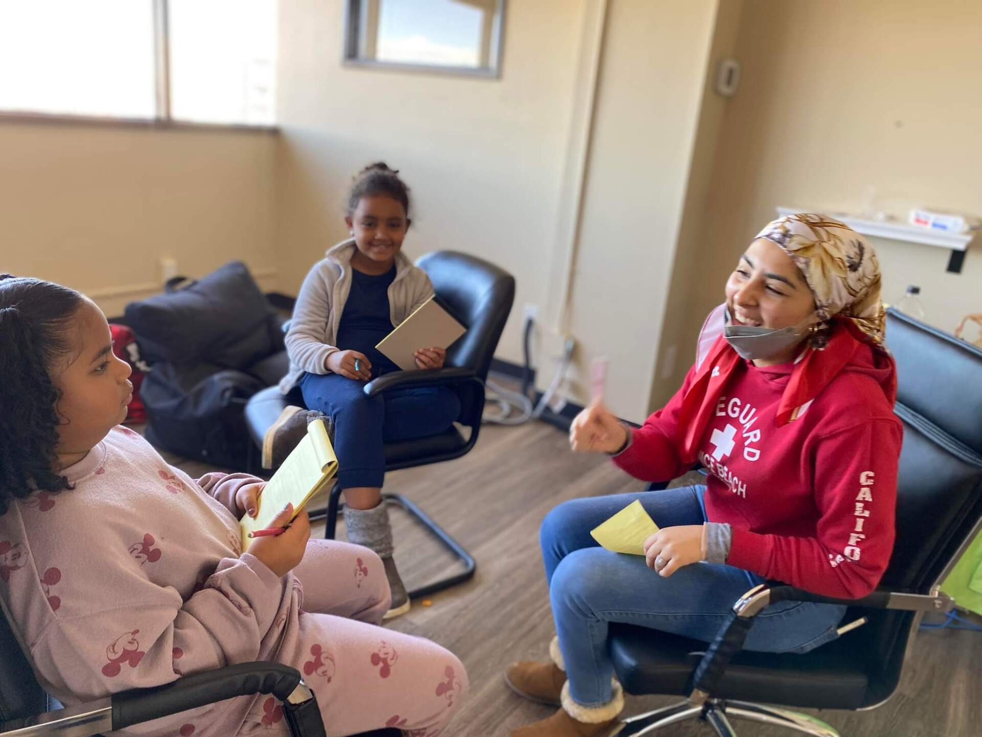 A group of women are sitting in chairs in a room talking to each other.