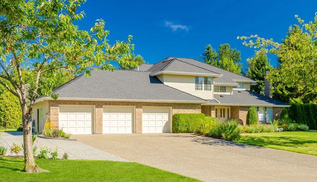 Suburban house with a large driveway, green lawn, and trees under a bright blue sky