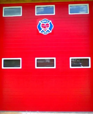 Red garage door with six small windows and a fire department emblem in the center