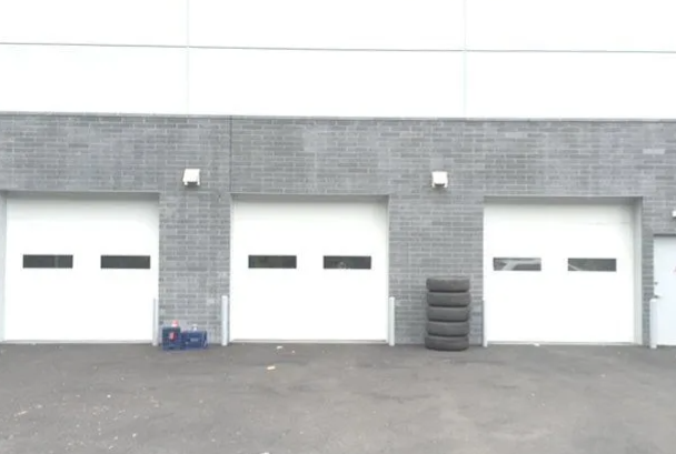 Three white garage doors in a gray brick industrial building with tires stacked by the right door.