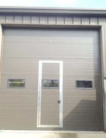 Gray industrial garage door with a centered pedestrian door and two narrow windows on each side.