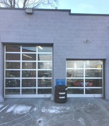 Two garage doors on a gray building with snow on the ground and a blue bin in front