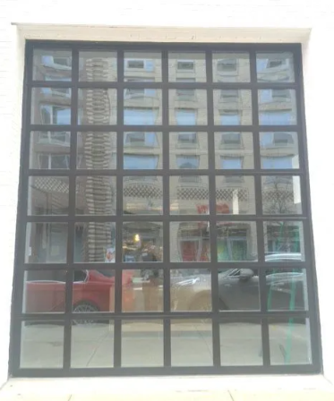 Modern building facade with large black-framed windows reflecting parked cars and nearby structures