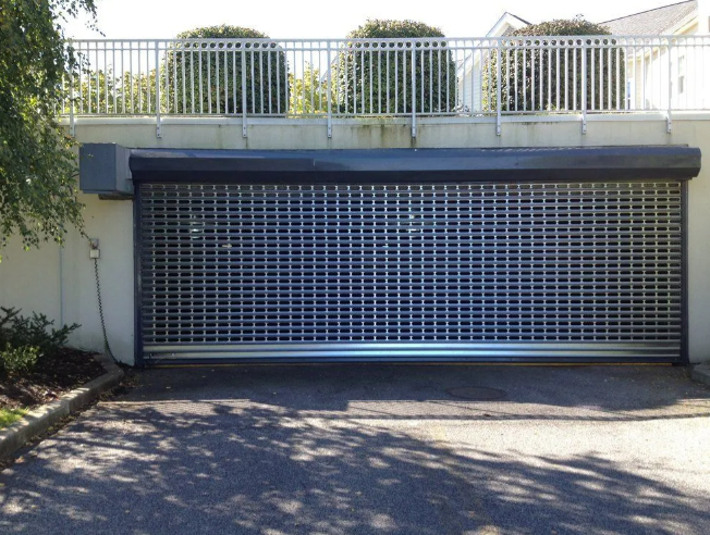 Closed metal garage door under a balcony with white railing, beside a driveway in sunlight