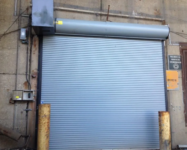 Closed blue-gray metal roll-up door on an industrial building exterior.
