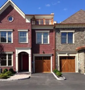 Row of modern brick-and-stone townhouses with garages and a driveway under a blue sky