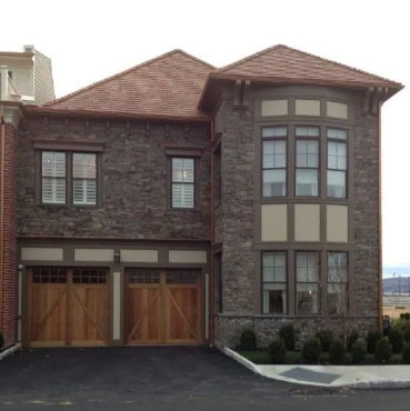 Modern two-story brick house with wood garage doors, tall front window, and dark shingle roof