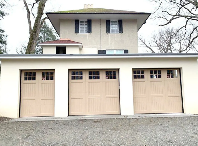 Three-car beige garage with second-story house above, set behind a gravel driveway.