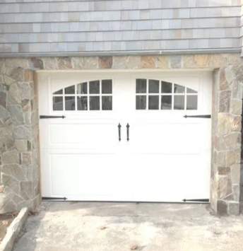 White double garage doors under a stone-trimmed house facade with small arched windows above