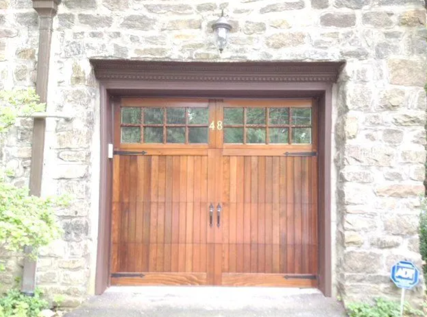 Wooden double doors set in a stone wall, with small windows above.