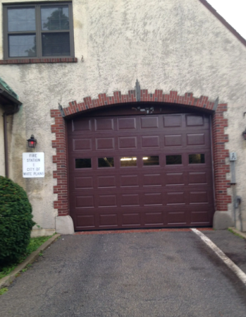 Maroon garage door with brick arch on a stucco house driveway