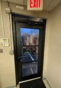 Glass exit door in a hallway, with a red EXIT sign above it and a city view outside.