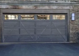 Gray double garage door set in a stone wall with small windows above and a blue wall light on the right