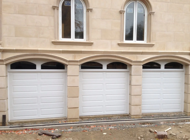 Three white garage doors on a beige stone building with arched windows above