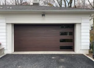 White garage with a dark brown door and three small windows, seen from a driveway