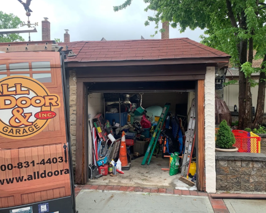 Open garage filled with tools and equipment beside an All Door & Garage service truck.