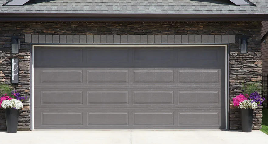 Gray double garage door on a stone house facade with potted flowers on both sides.