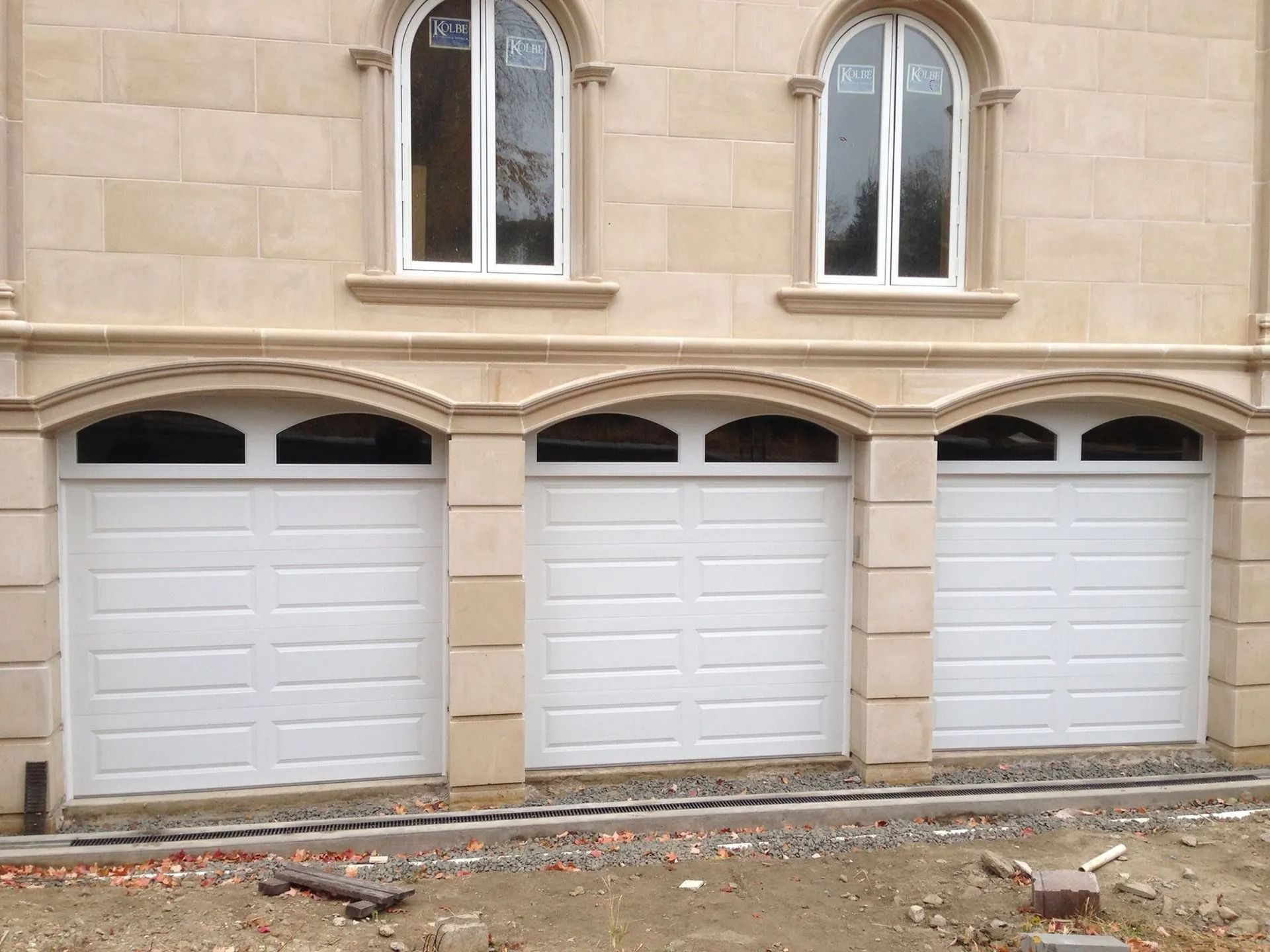 Three white garage doors in a tan stone building facade