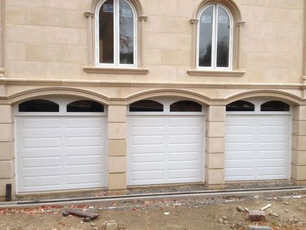 Three white garage doors in a tan stone building facade