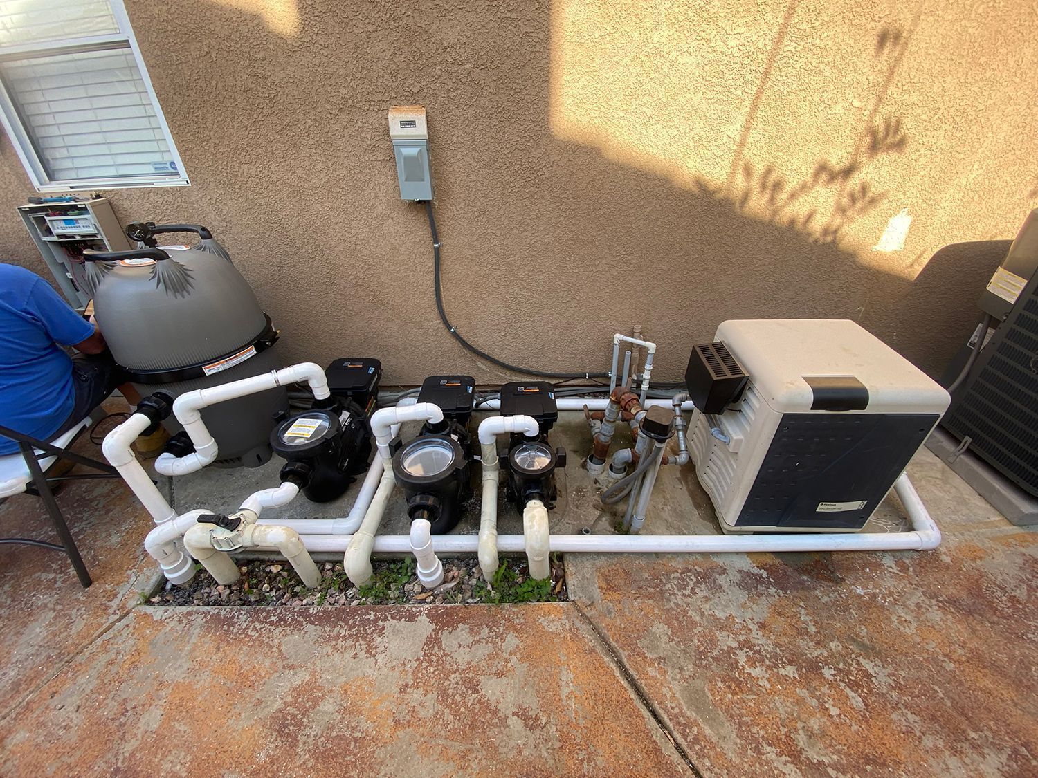 Pool equipment setup with pumps, filter, and heater against a textured wall.