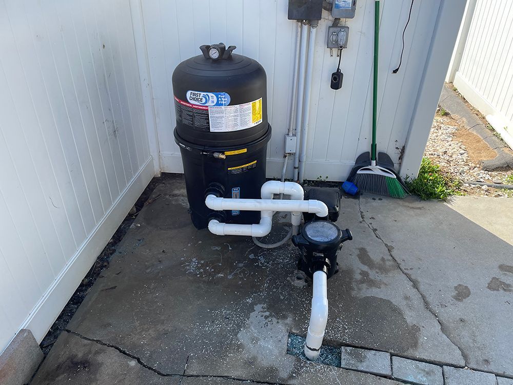 Pool pump system: black filter and pump, white pipes, concrete ground, outdoor.