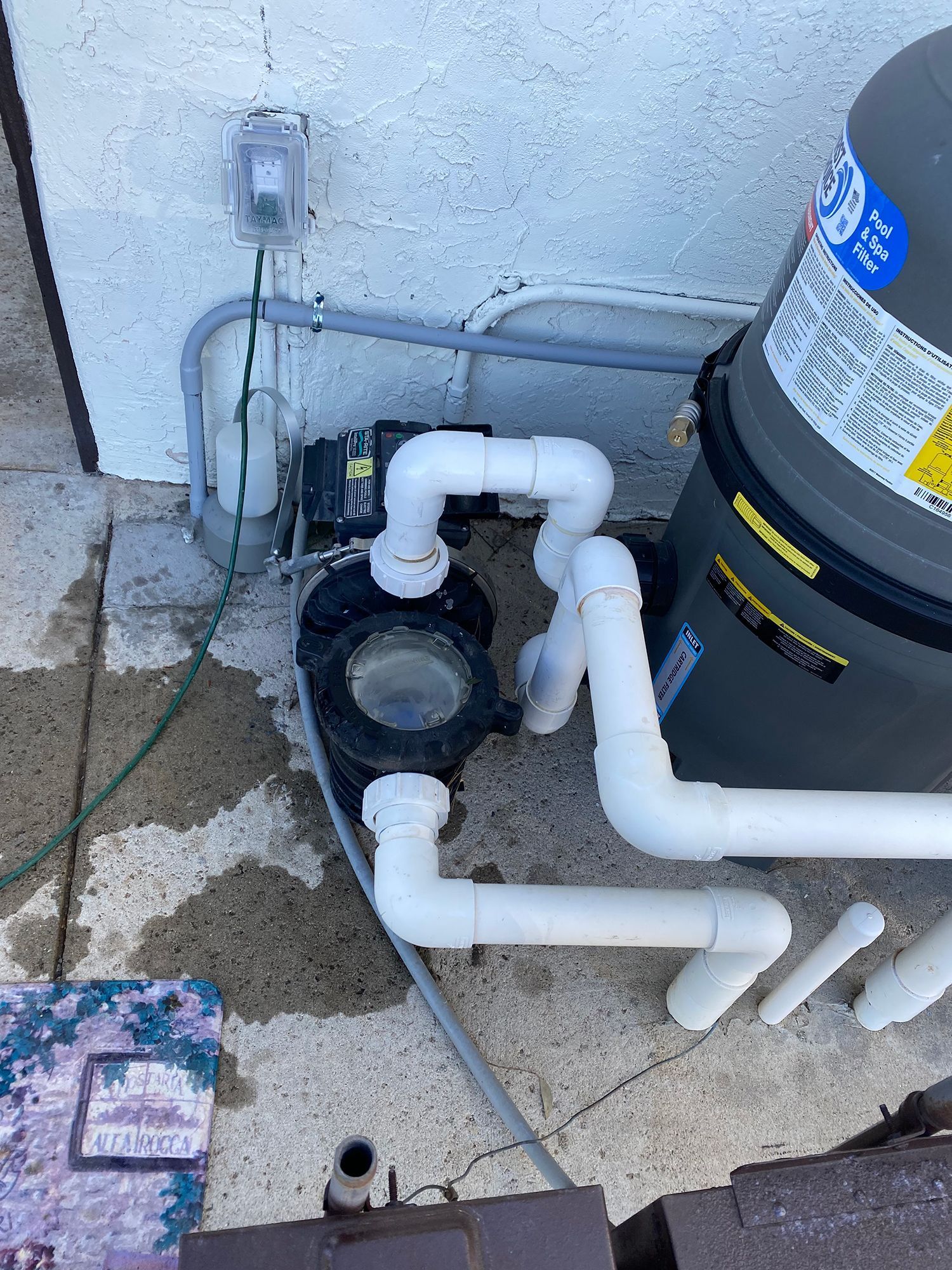 Pool pump and filter system with white pipes and electrical wiring against a white stucco wall.