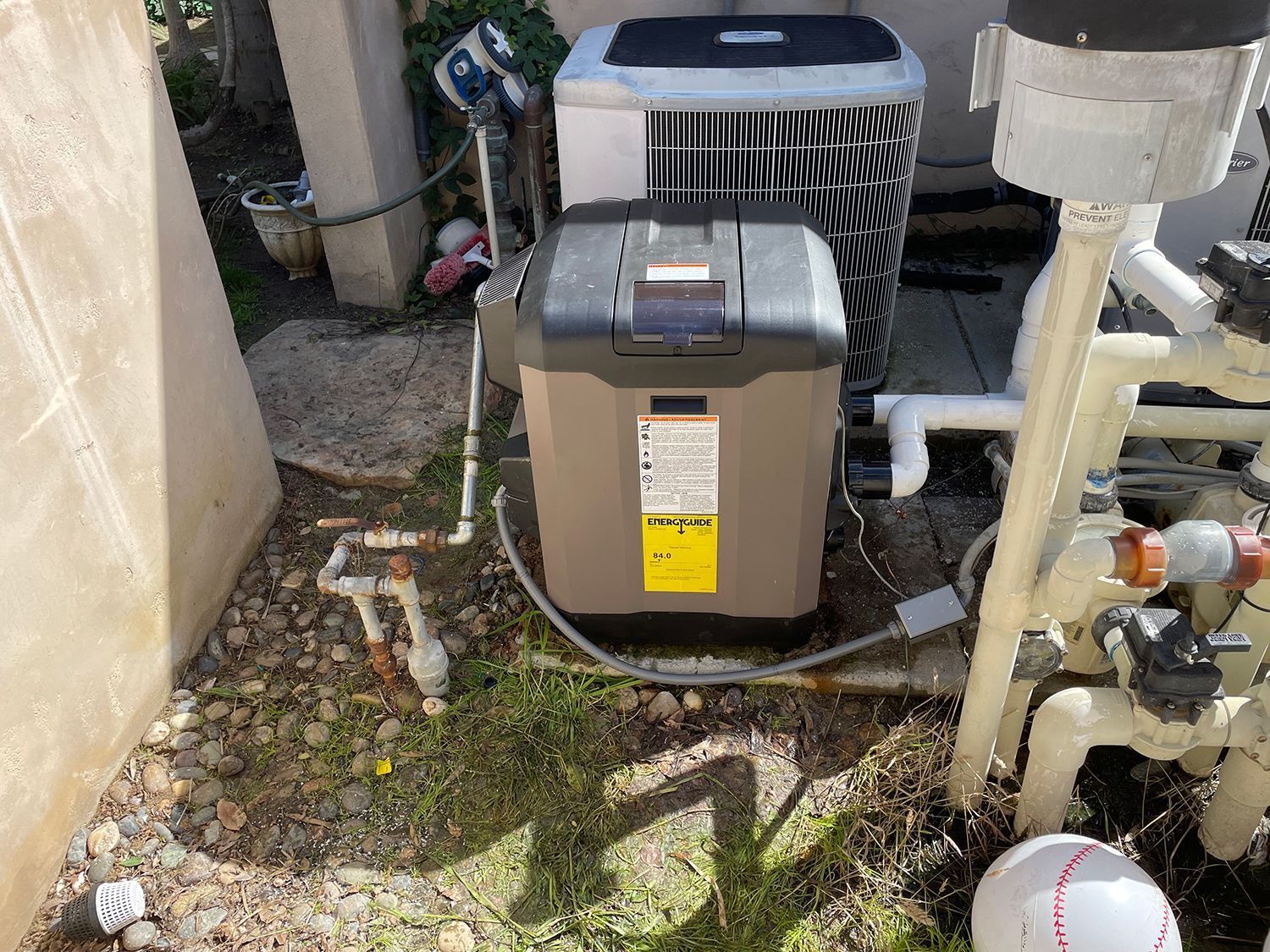 Pool heater next to an air conditioning unit, outdoors. Beige and black equipment on gravel.