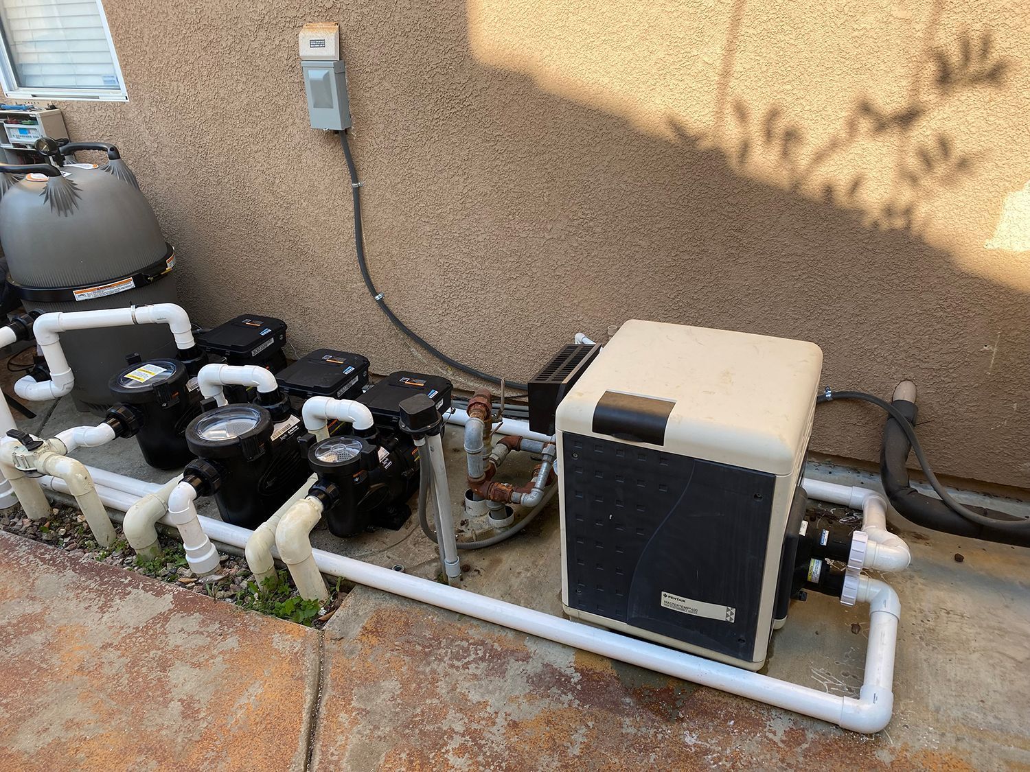 Pool equipment: heater, pumps, filter, and plumbing against a stucco wall.