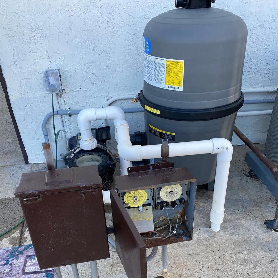 Pool equipment setup: pump, filter, timer boxes, and plumbing against a wall.