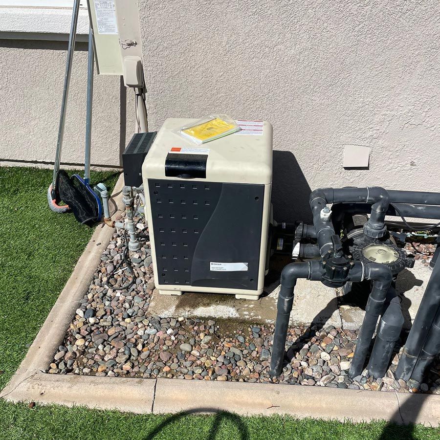 Pool heater and plumbing next to a beige building on gravel and grass.
