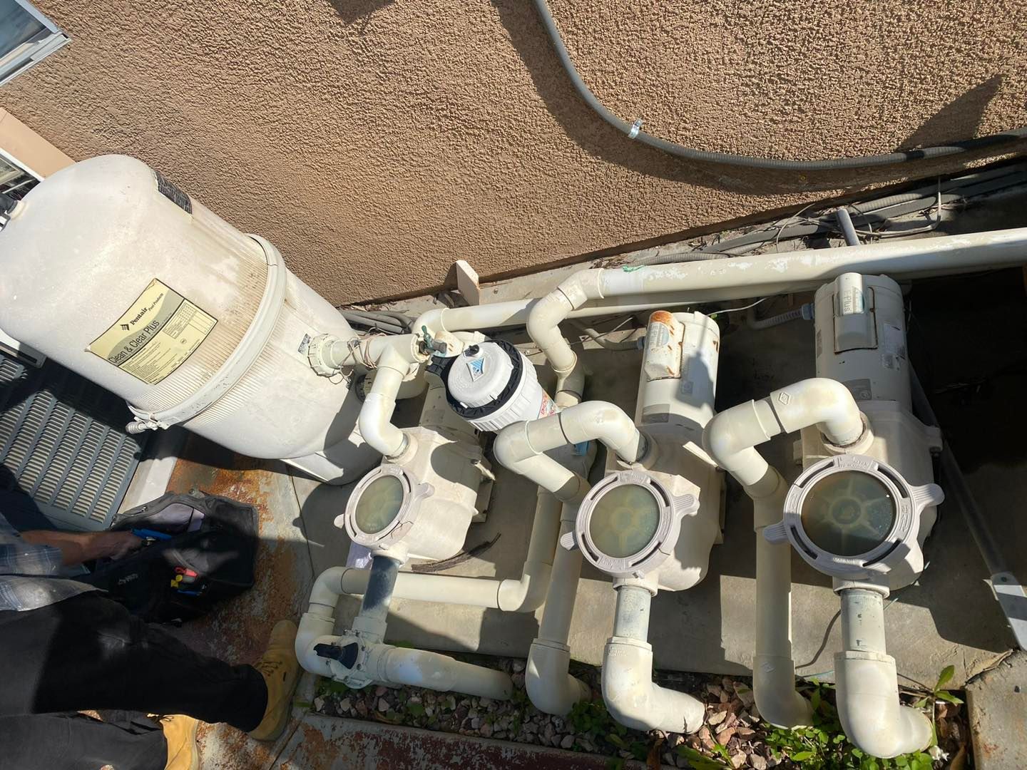 Pool equipment, including a filter and lights, on a concrete surface. White pipes and tanks.