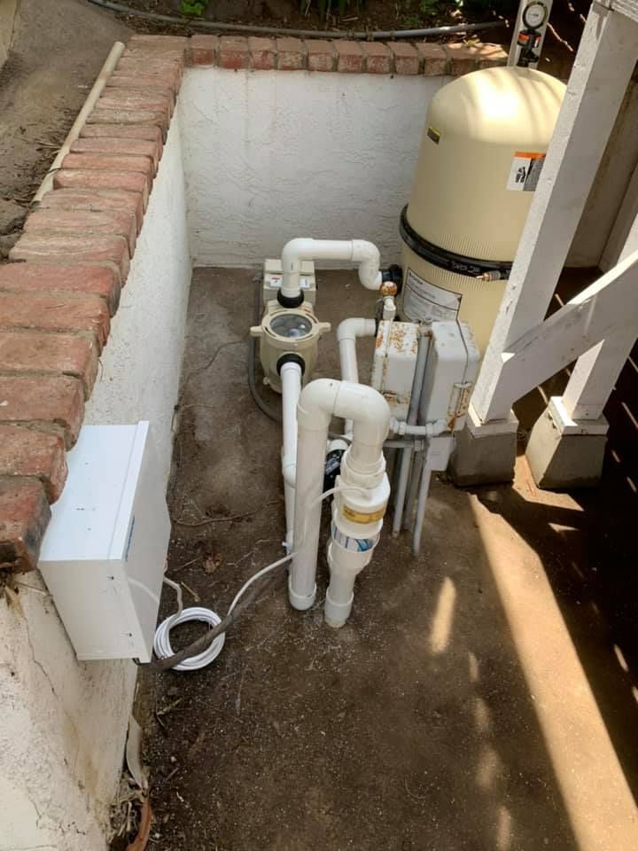 Pool pump and filter equipment in a small, enclosed area with white and tan elements.