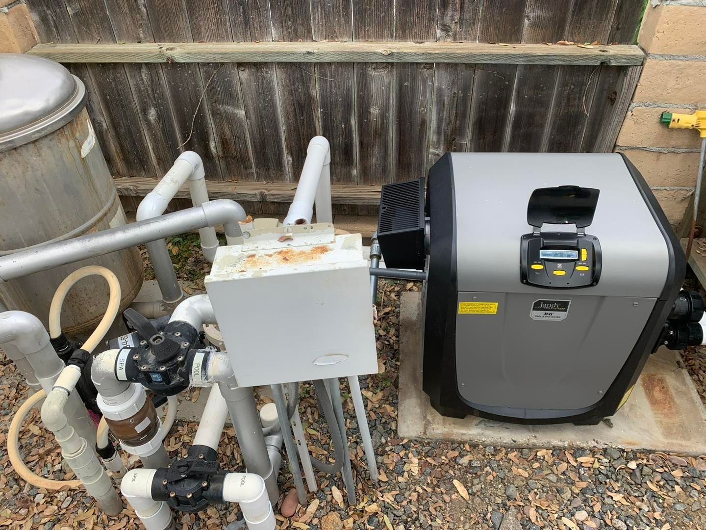 Pool equipment: filter, heater, control box, and piping, in a backyard setting.