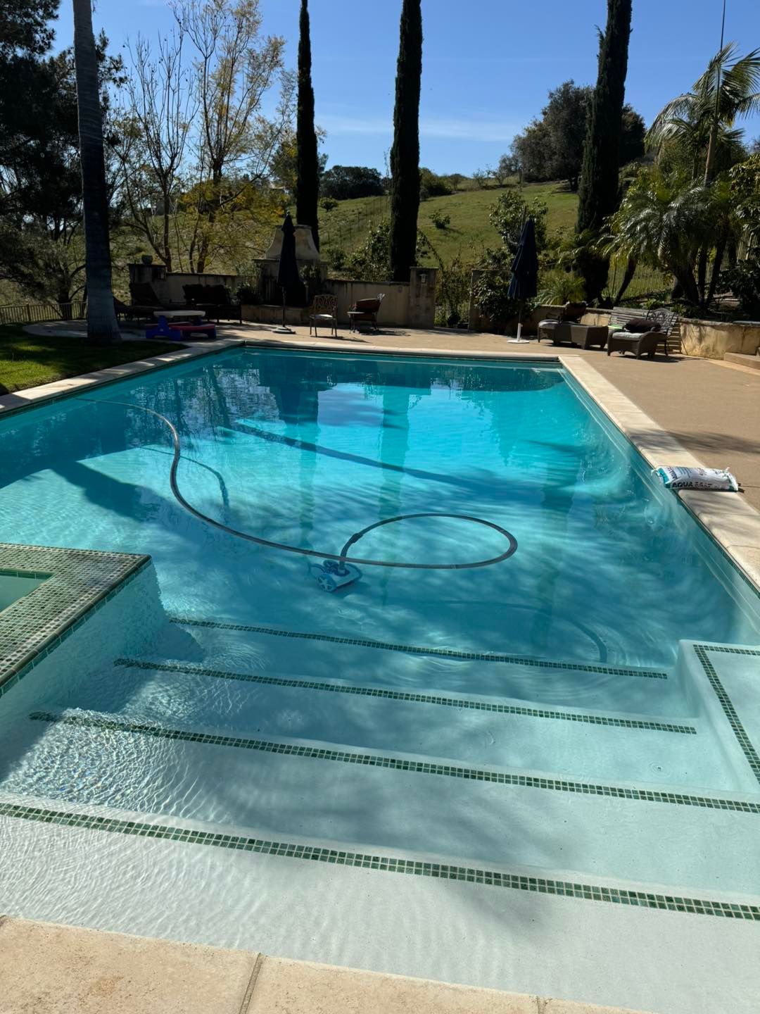 Pool with steps, blue water, and a robotic cleaner; outdoor setting on a sunny day.