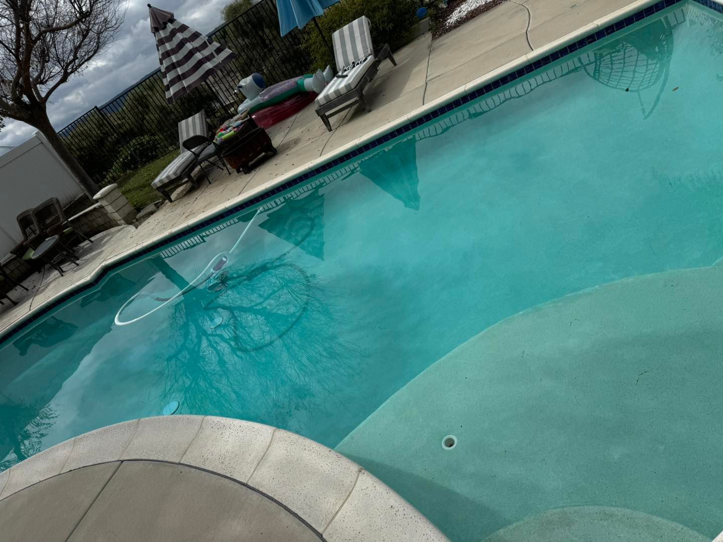 Swimming pool with clear blue water, lounge chairs, and a striped umbrella.