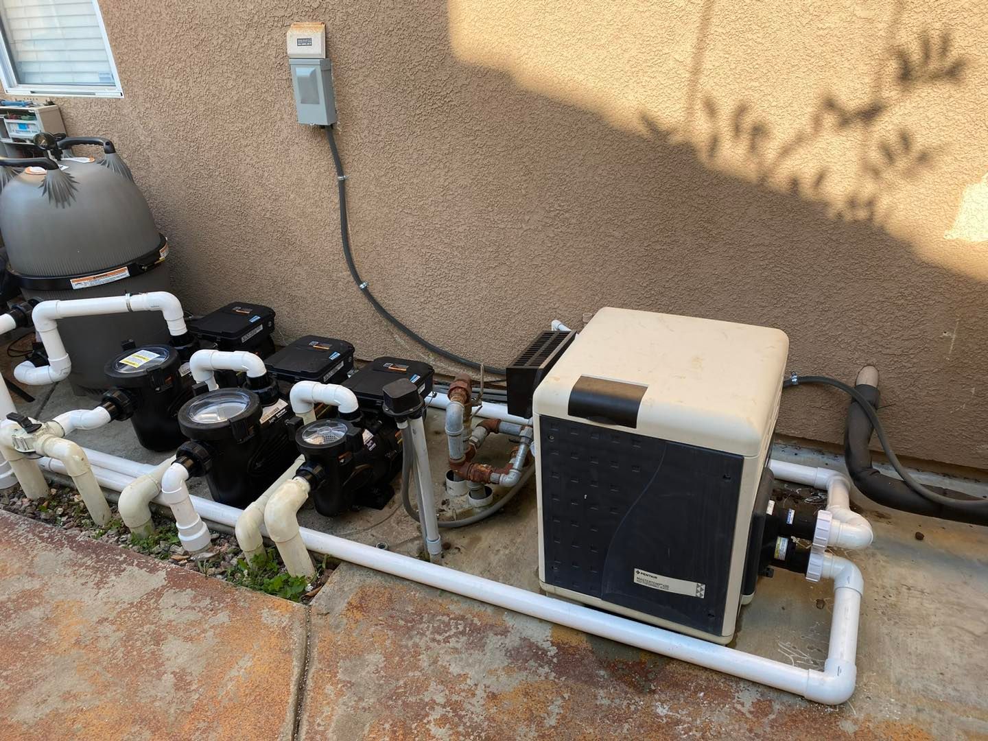 Pool equipment: filter, pumps, heater, and pipes against a stucco wall.