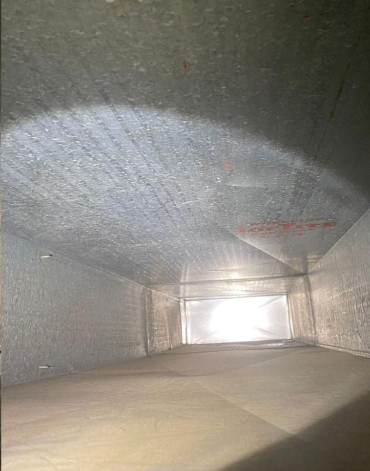 Interior view of a rectangular, metal air duct, with visible dust and a bright light source at the far end.