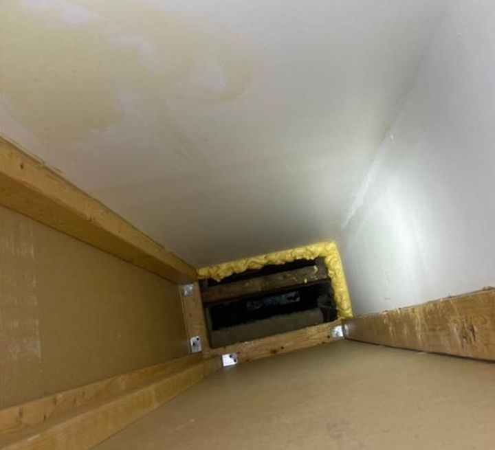 Interior view of a rectangular duct, showing insulation, wood framing, and discoloration on the ceiling.