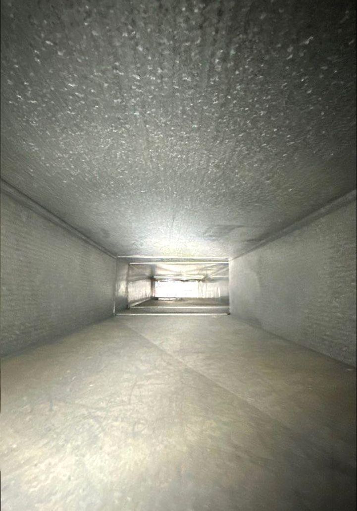 Inside view of a rectangular, metal ventilation duct. Walls are gray and dusty, receding into the distance.