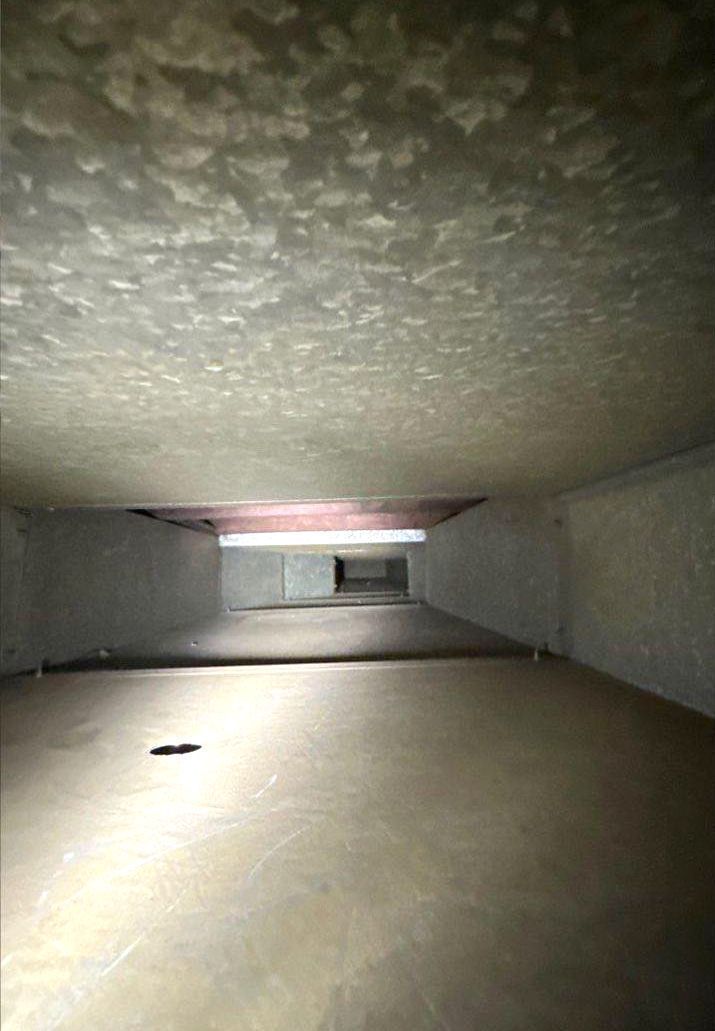 Inside view of an air duct, rectangular with textured, light-colored walls and ceiling; rectangular opening ahead.