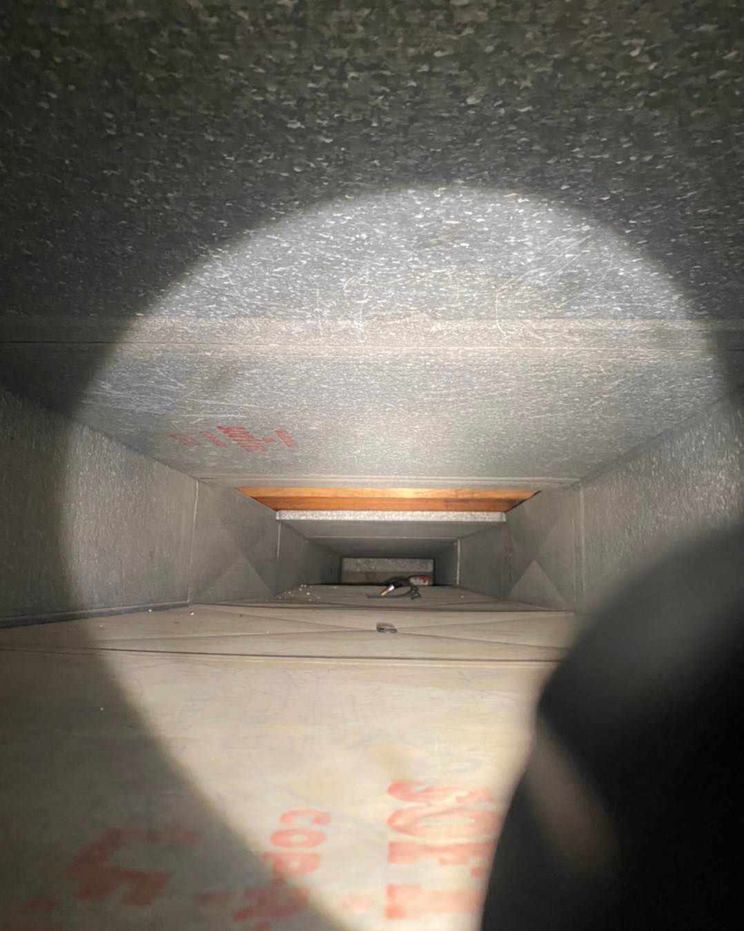 Inside of rectangular air duct, gray metal walls, lit by a flashlight.